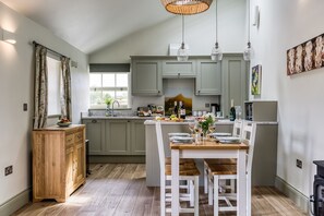 A modern kitchen with a dining area, wooden cabinets, a window, and a dining table set for a meal. - Billy Goats Gruff - Bakewell , Derbyshire (Bakewell)