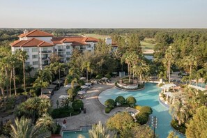 Un complexe hôtelier doté d’une grande piscine, de palmiers et, au loin, d’un terrain de golf.