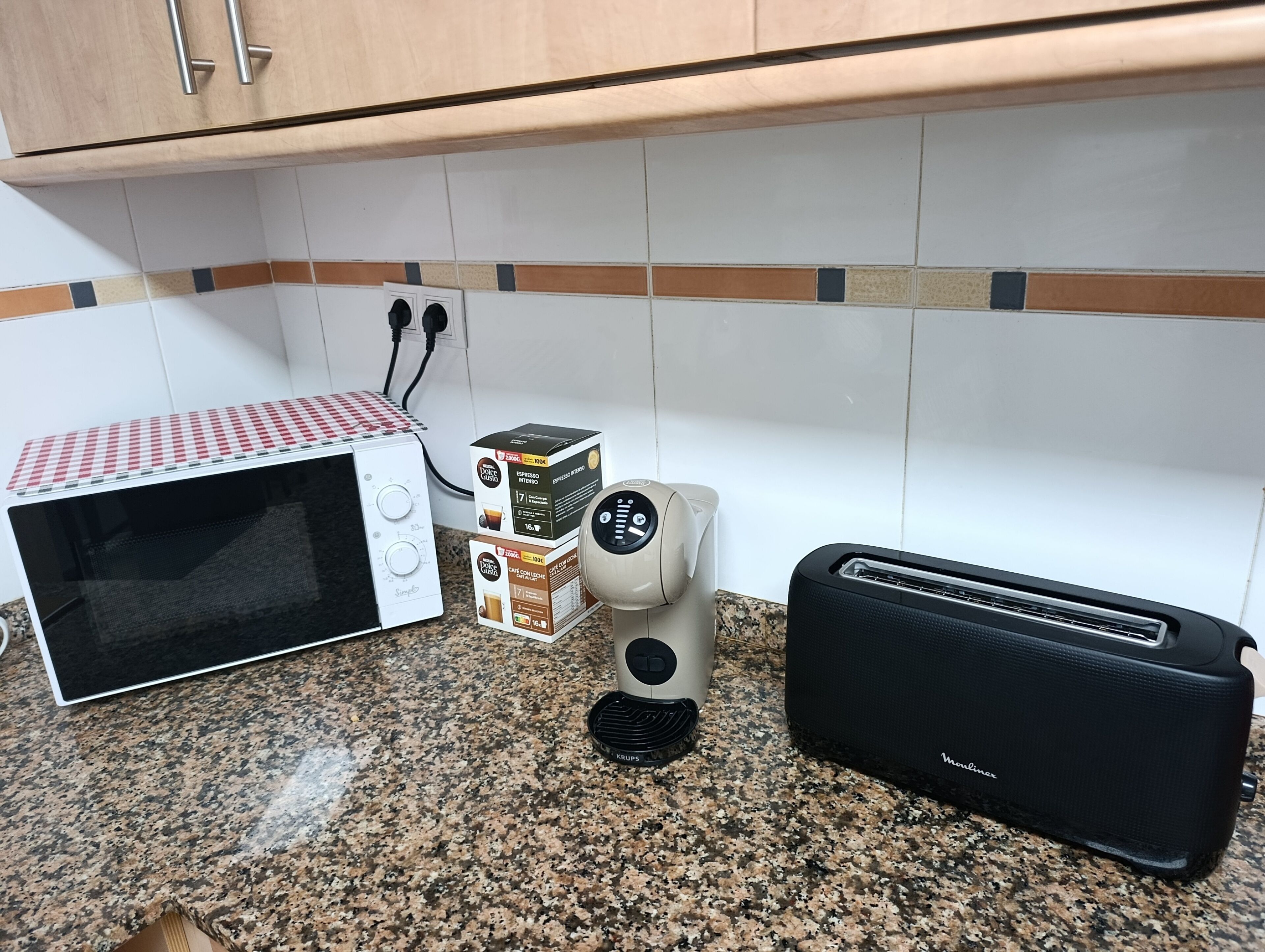 Ett kök med mikrovågsugn, kaffebryggare och brödrost på en bänkskiva av granit.