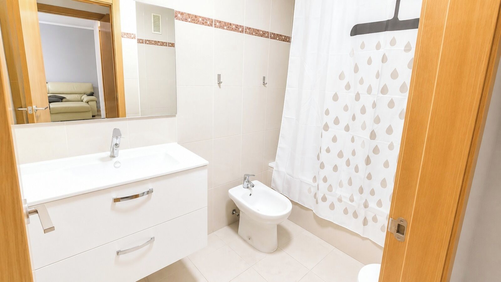 Une salle de bain avec un lavabo blanc, un bidet et un rideau de douche orné d’un motif de feuilles.