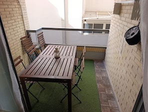 Eine kleine Terrasse im Freien mit einem Holztisch und Stühlen, einem Laternen und einer Backsteinmauer.