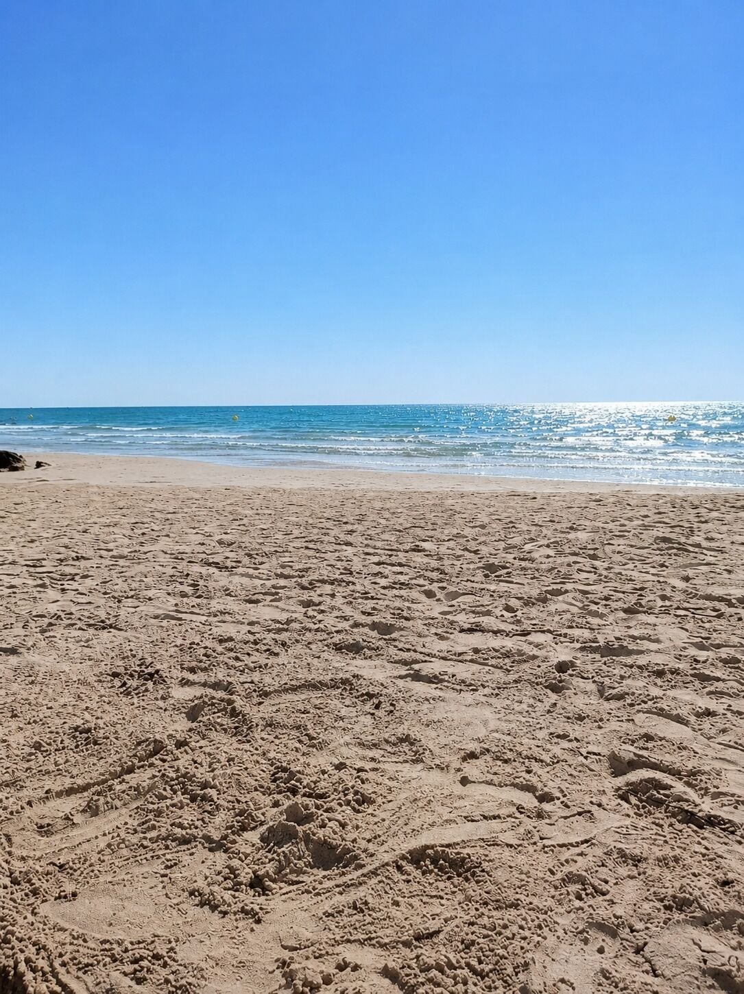 Una playa con surcos de neumáticos e huellas en la arena.