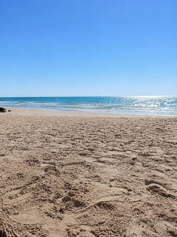 A beach with visible tire tracks and footprints in the sand.