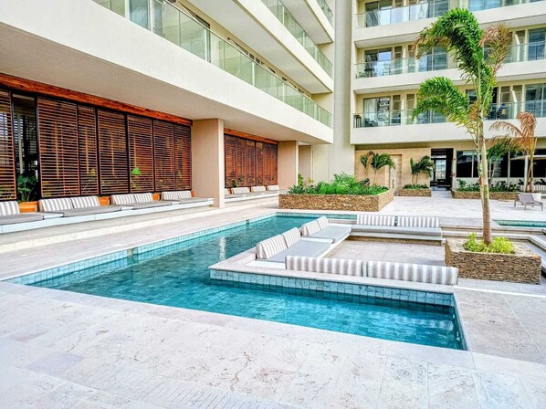Atrio moderno di un hotel con piscina centrale, zone relax e un edificio a più piani con balconi.