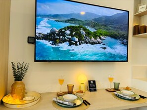 Ein Fernseher zeigt eine malerische Landschaft, ein Tisch ist mit Tellern, Gläsern und Kerzen gedeckt, und ein Schild weist auf eine Reservierung hin.