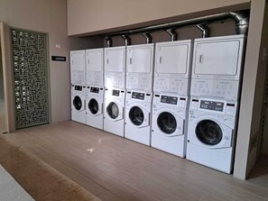 A row of white laundry machines with control panels, arranged in a row against a wall.