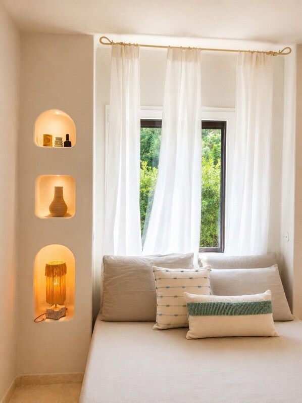 A bedroom with a bed, white curtains, and wall-mounted shelves with decorative items. - Sunset Suite Sardinia 1.5 (Porto Rotondo)