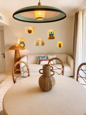 A dining area with a round table, wicker chairs, a woven vase centerpiece, and a hanging light fixture above. - Sunset Suite Sardinia 1.5 (Porto Rotondo)