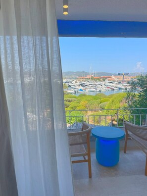 A balcony with a view of a marina and boats, a round blue table, and wicker chairs. - Sunset Suite Sardinia 1.5 (Porto Rotondo)
