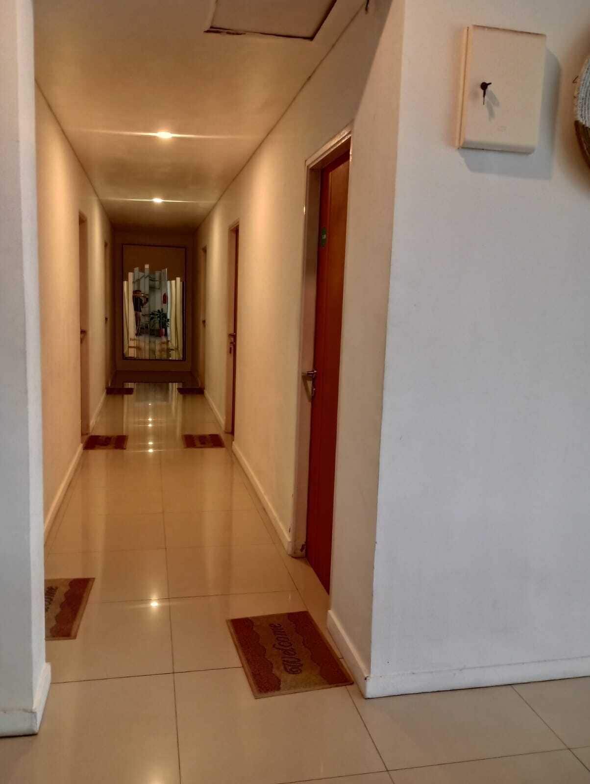 Corredor de hotel com chão ladrilhado, portas vermelhas e tapete de boas-vindas.