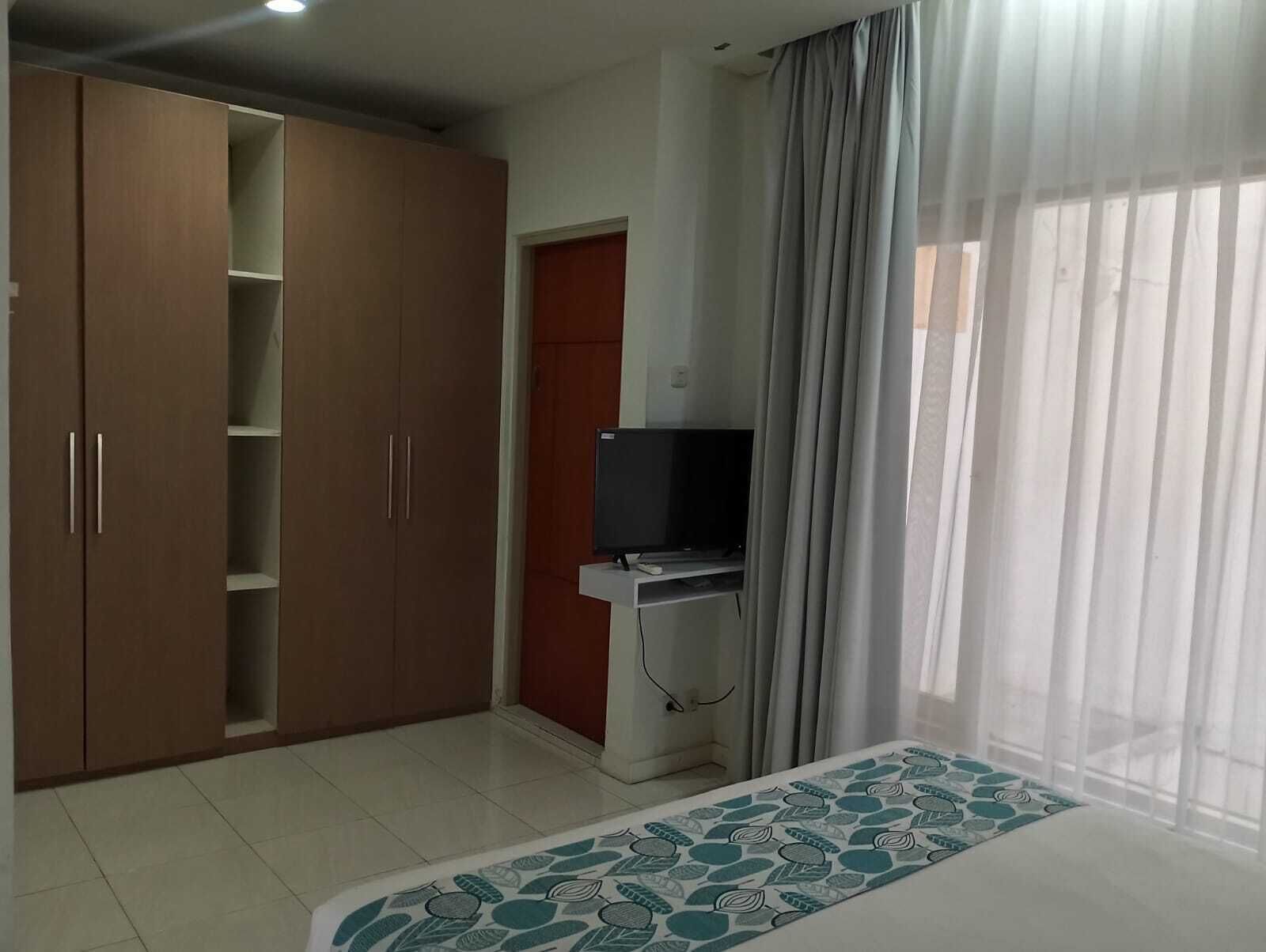 Quarto com armário, televisão e janela com cortinas.