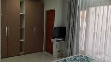 Quarto com armário, televisão e janela com cortinas.