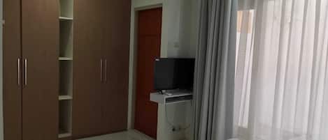 A room with a wardrobe, a television, and a window with curtains.