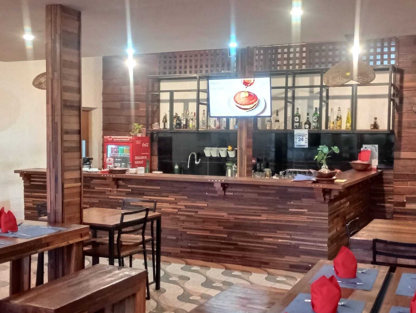 Uma área de bar com mobiliário de madeira, um balcão com tela de TV e prateleiras com garrafas.