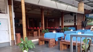 An outdoor seating area with tables and benches, a bamboo pillar, and a sign for 'Gossip Lounge'. - new poppies hotel (Senggigi)
