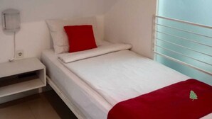 Une chambre avec un lit superposé, un lit simple en bas et une table de chevet blanche avec une lampe.