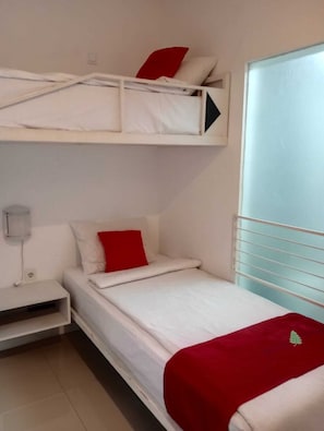 A bunk bed room with a single bed below and a white nightstand with a lamp.