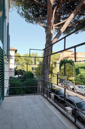 A balcony with a metal railing, a tree, and a view of parked cars and buildings in the background. - Casa e Appartamento Vacanze Gallese 7 (Roma)