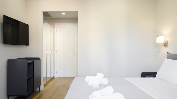 Habitació d'hotel amb un llit, una televisió, un armari i un bany visible a través d'una porta oberta.