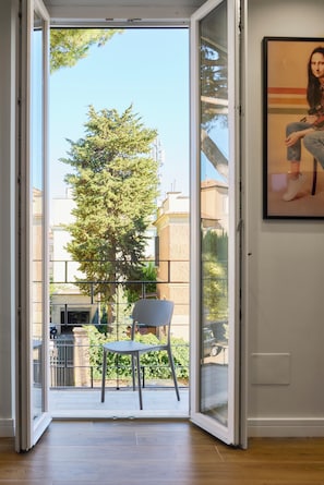 Eine offene Glastür, die auf einen Balkon mit einem Stuhl und einem Baum führt.