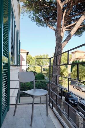 Ein Balkon mit Stuhl, Baum und Blick auf die Straße.