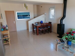A dining area with a table and chairs, a black stove, a window with a view, and a door. - Cosy villa on Rhodes w/garden, orchard and panoramic view of the Aegean Sea! (Afantou)