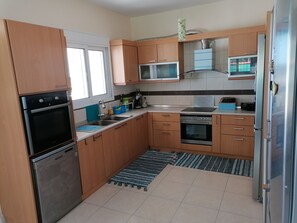 A compact kitchen with wooden cabinets, a stainless steel refrigerator, a microwave, and a dishwasher. - Cosy villa on Rhodes w/garden, orchard and panoramic view of the Aegean Sea! (Afantou)