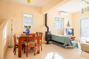 A cozy living room with a dining area, a large window, a fireplace, and a television. - Cosy villa on Rhodes w/garden, orchard and panoramic view of the Aegean Sea! (Afantou)