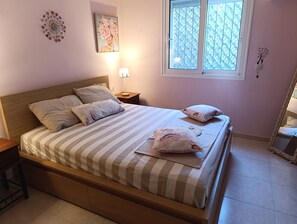 A bedroom with a bed, pillows, a nightstand, a lamp, a window, and a wall decoration. - Cosy villa on Rhodes w/garden, orchard and panoramic view of the Aegean Sea! (Afantou)