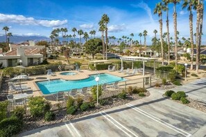 A swimming pool with lounge chairs and a covered area, surrounded by palm trees and residential buildings. - 2BR Condo w/ Resort-Style Amenities (Palm Desert)