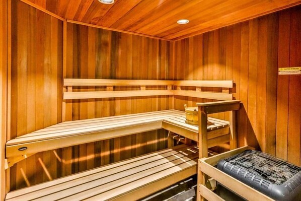 Una sauna in legno con panche e una seduta, un tavolo in legno e un riscaldatore.