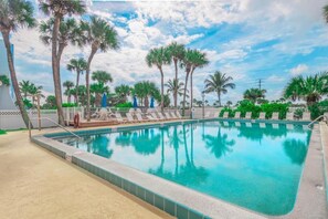 Une piscine avec des chaises longues, des palmiers et un ciel dégagé.