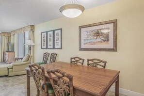 Un coin repas avec une table et des chaises en bois, des œuvres d’art encadrées au mur et une lampe.