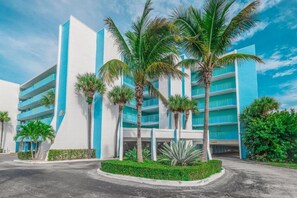 Un hôtel moderne à la façade bleue et blanche, avec de nombreux étages et des palmiers au premier plan.