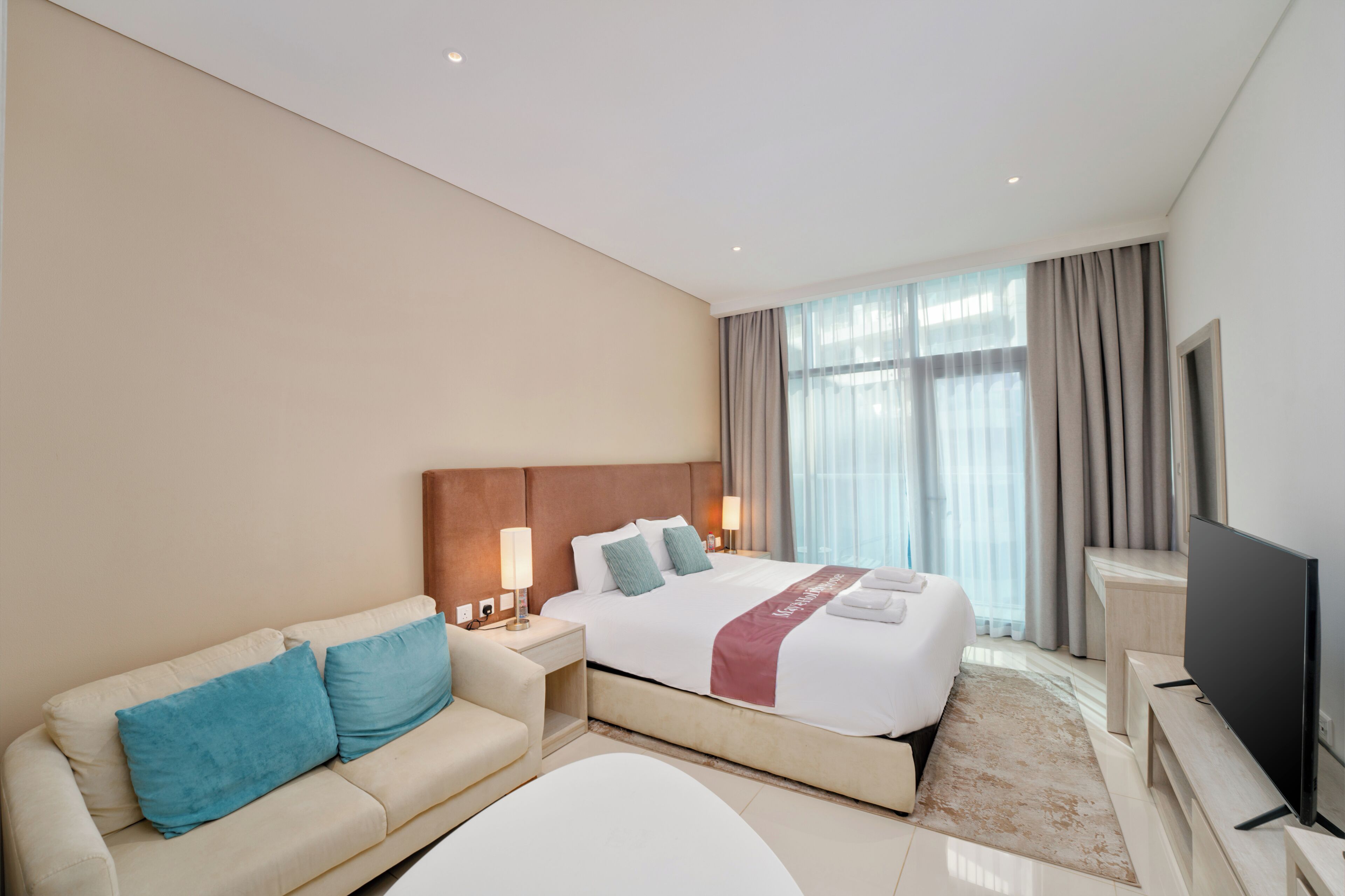 A hotel room with a bed, a sofa, a TV, and a window with curtains.