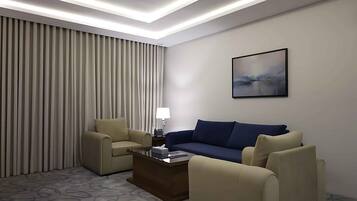 A hotel room with a beige sofa, a blue sofa, a coffee table, and a painting on the wall.