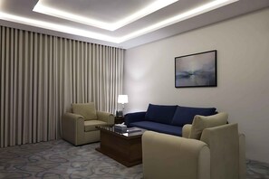 A hotel room with a beige sofa, a blue sofa, a coffee table, and a painting on the wall.