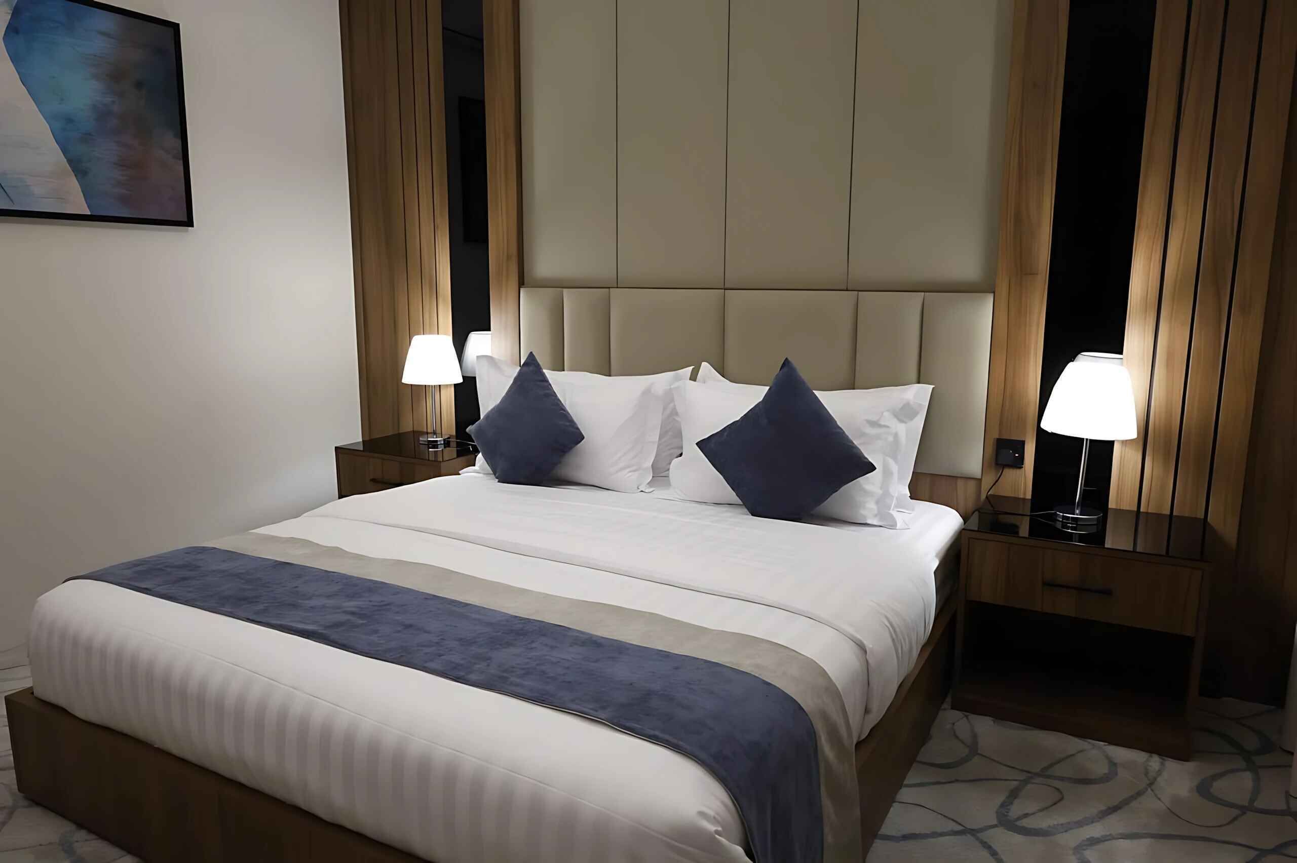 A hotel room with a large bed, two bedside tables, a headboard, and a painting on the wall.