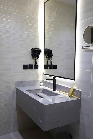 A modern bathroom with a white sink, a black faucet, and a large mirror.