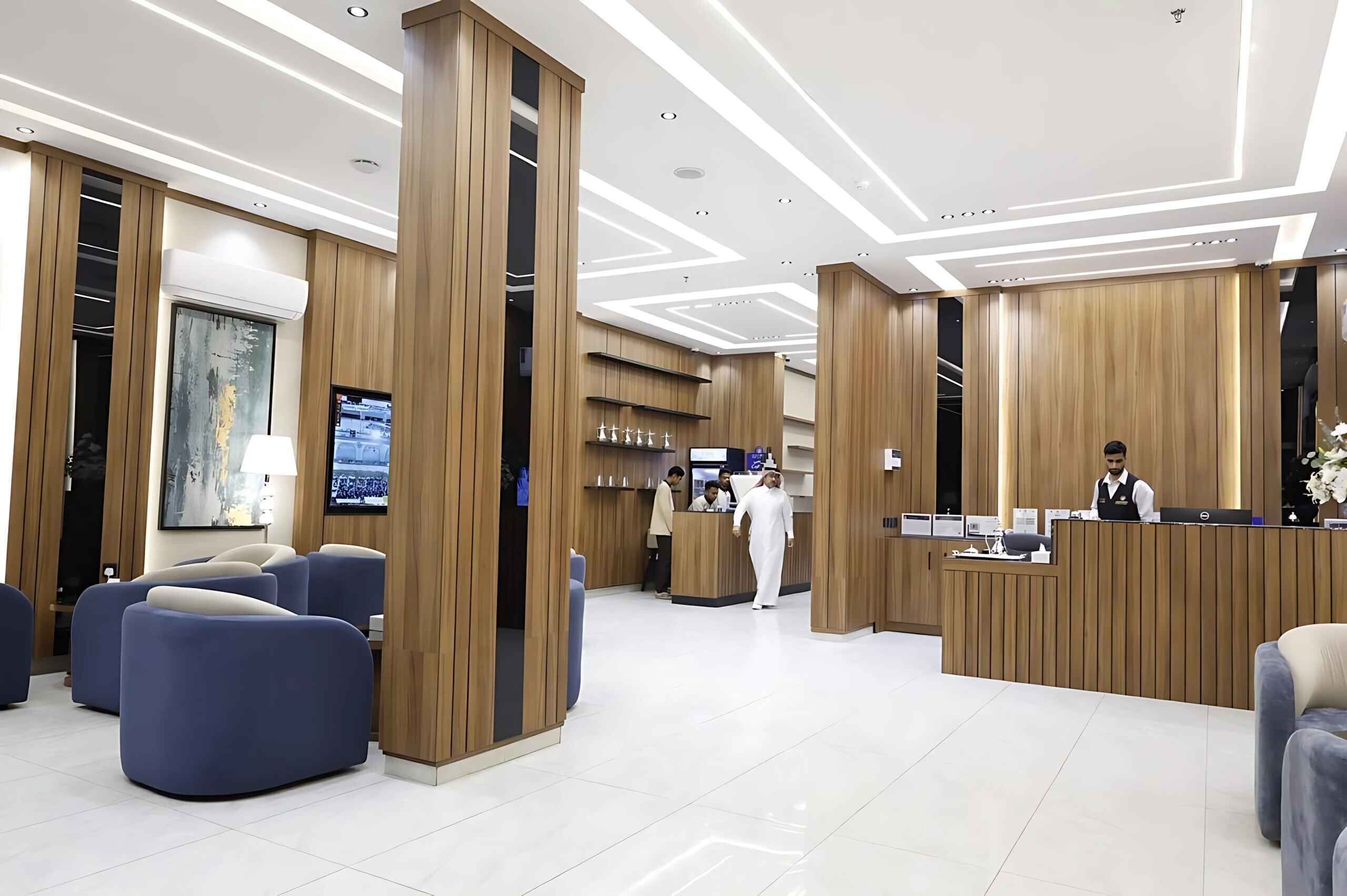 A hotel reception area with a modern design, featuring a reception desk, seating area, and a television screen.
