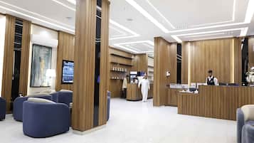 A hotel reception area with a modern design, featuring a reception desk, seating area, and a television screen.