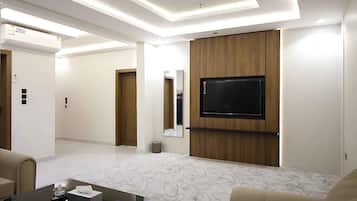 A modern hotel room with a flat-screen TV mounted on a wooden panel, a marble-patterned floor, and a sofa.