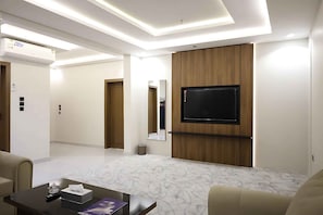 Una habitación de hotel moderna con un televisor de pantalla plana montado en un panel de madera, suelo con diseño de mármol y un sofá.