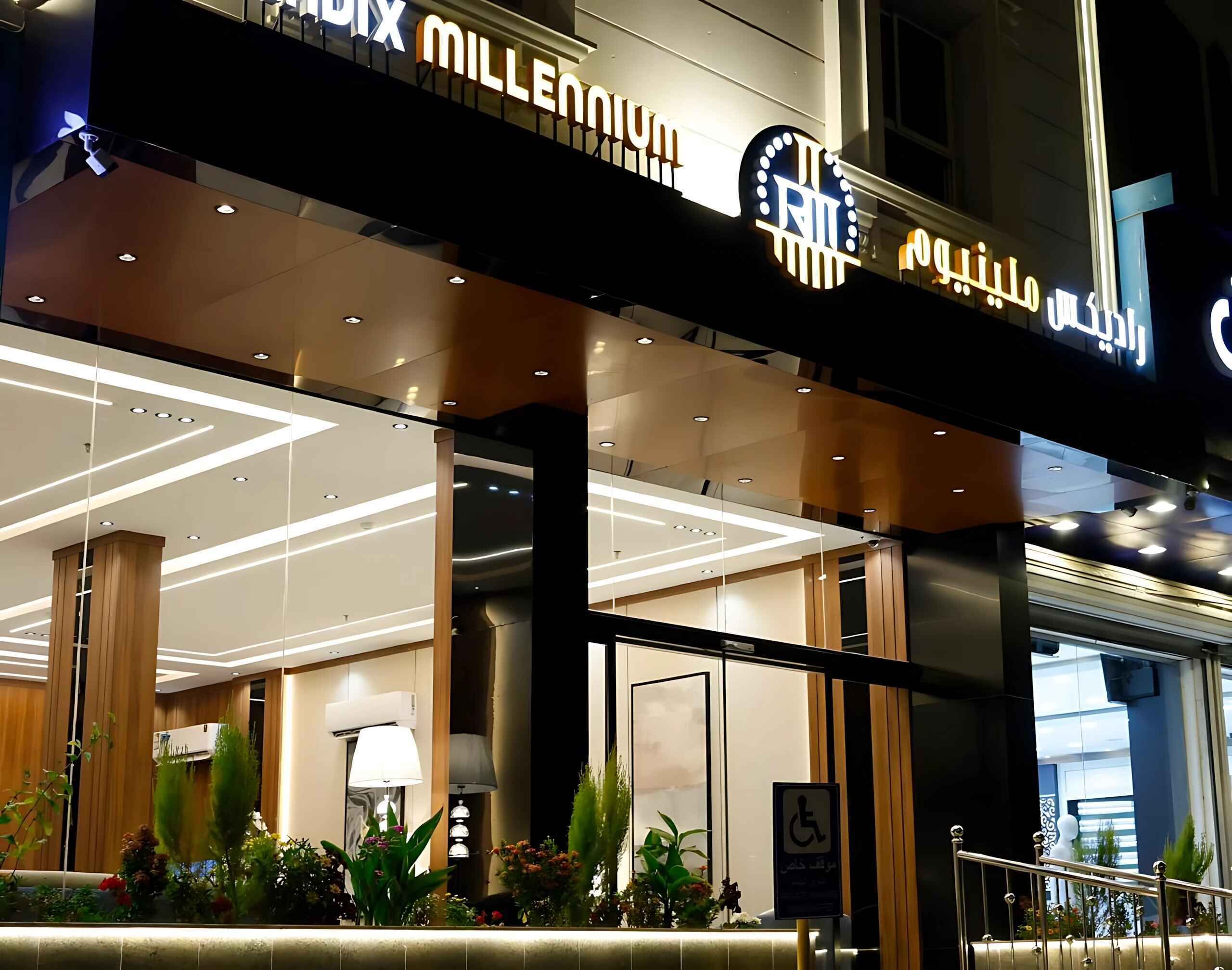A hotel entrance with a modern design, featuring a prominent sign with illuminated letters, a reception area with a desk, and a wheelchair accessibility sign.