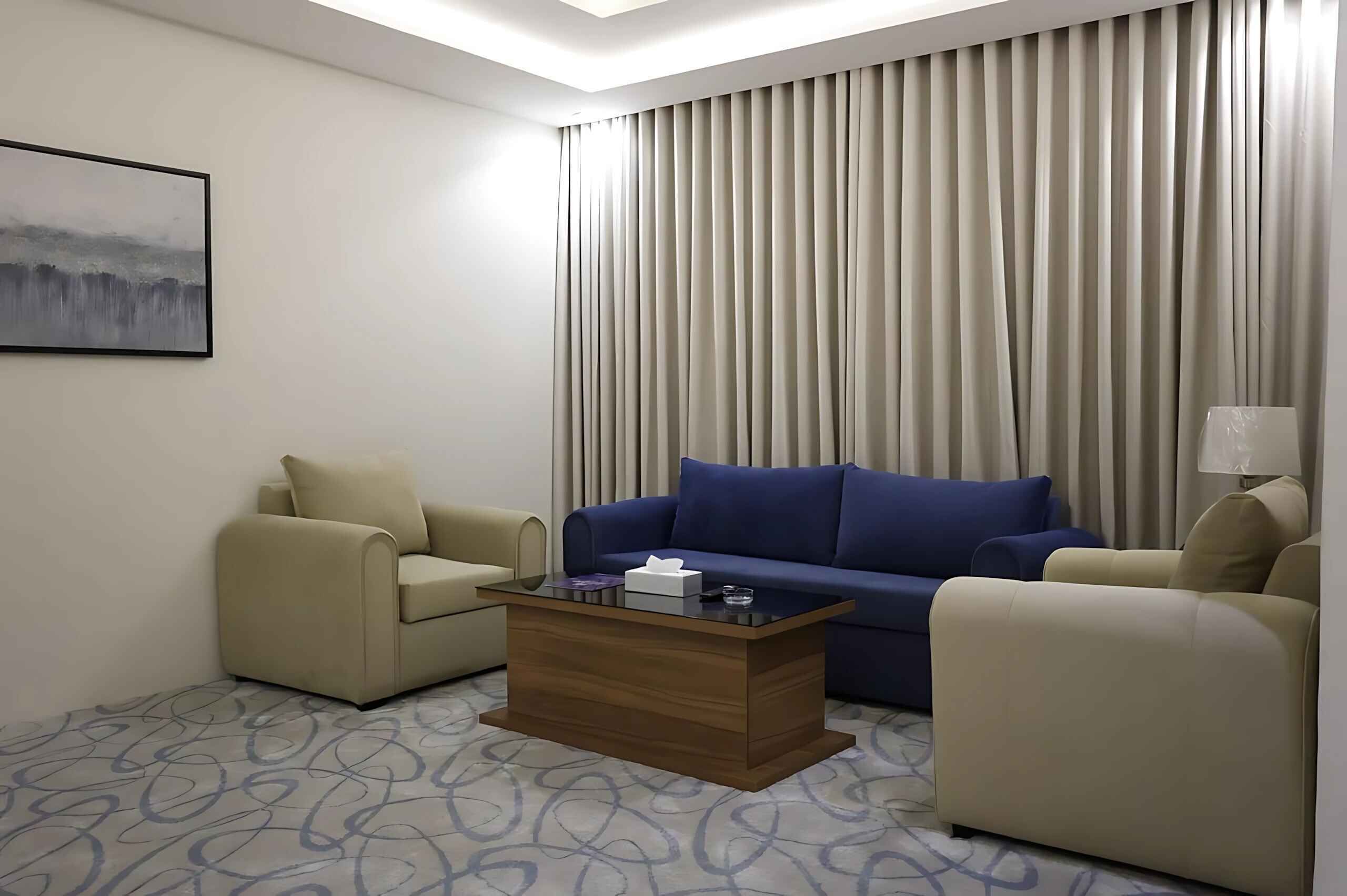 A hotel room with a sofa, two armchairs, a coffee table, a painting on the wall, and a window with curtains.