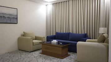 A hotel room with a sofa, two armchairs, a coffee table, a painting on the wall, and a window with curtains.