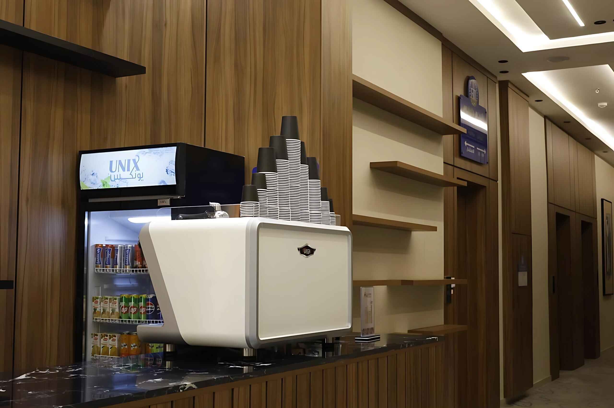 Un área de recepción con mostrador, un televisor mostrando la marca 'UNIX' y un dispensador de bebidas.
