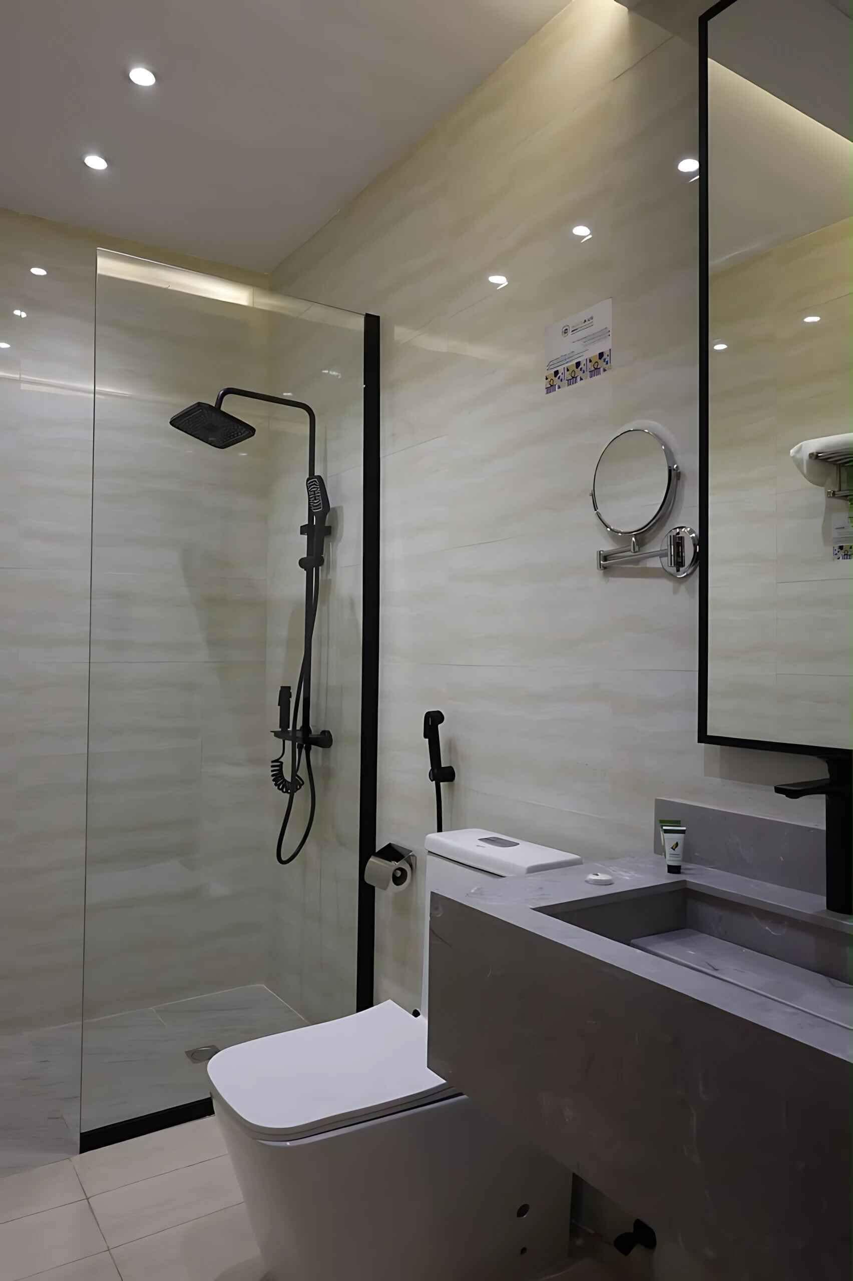 Un baño moderno con ducha de vidrio, lavamanos blanco y un espejo grande.