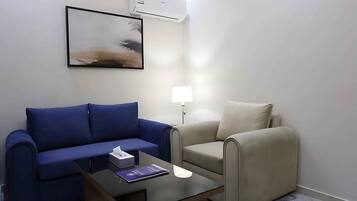 A hotel room with a blue sofa, a beige armchair, a small table with a lamp, and a framed picture on the wall.