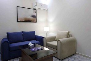 A hotel room with a blue sofa, a beige armchair, a small table with a lamp, and a framed picture on the wall.